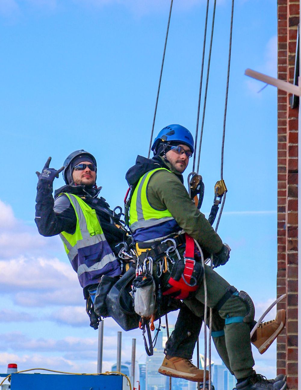 Two workers suspended in full body harnesses on a building facade