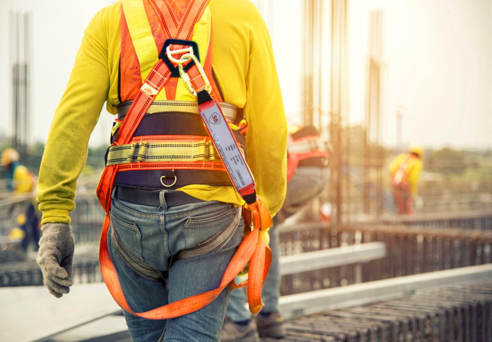 Worker wearing an SB full body harness with energy-absorbing lanyard on a construction site at sunrise